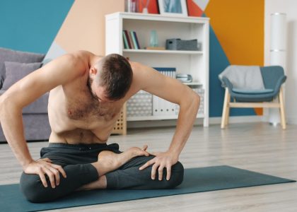 Topless guy is execising abdomen muscles practising yogic breathing technique at home sitting on yoga mat moving belly. People and healthy lifestyle concept.